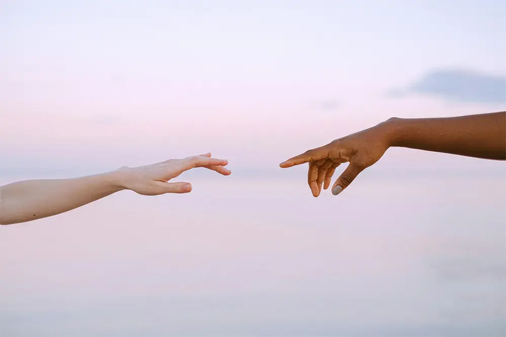 Two hands reaching towards each other against a soft dawn sky